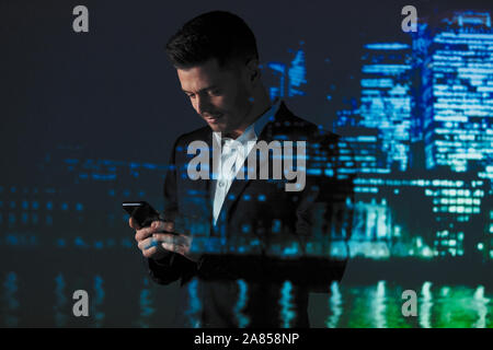 La doppia esposizione imprenditore utilizzando smart phone contro highrise luci di notte Foto Stock