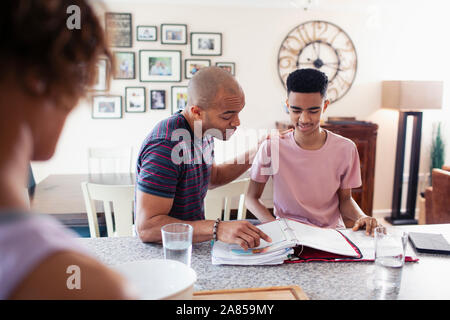 Padre aiutare nostro figlio adolescente con i compiti in cucina Foto Stock