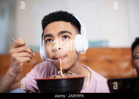 Ragazzo adolescente con cuffie mangiare tagliatelle Foto Stock