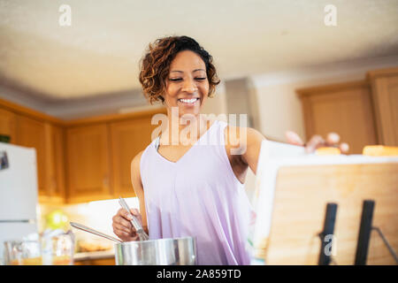 Donna sorridente con il libro di cucina in cucina Foto Stock