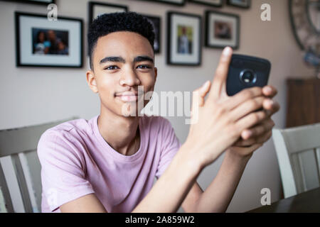 Ritratto fiducioso ragazzo adolescente utilizzando smart phone Foto Stock