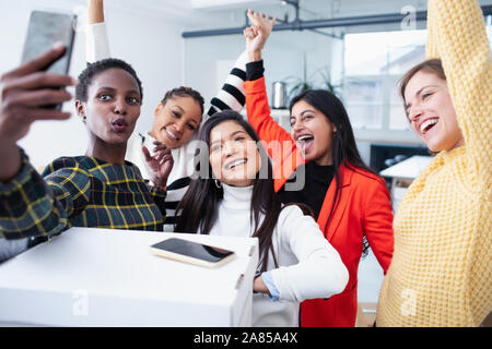 Felice imprenditrici che celebra un nuovo ufficio, tenendo selfie Foto Stock