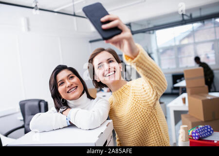 Sorridente imprenditrici tenendo selfie nel nuovo ufficio Foto Stock