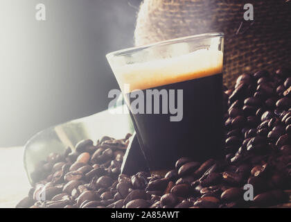 Caffè espresso in tazza di vetro con i chicchi di caffè sul tavolo di legno. Foto Stock