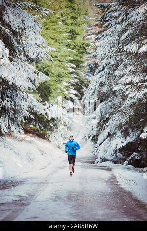 Uomo di jogging sul sentiero nel bosco innevato Foto Stock