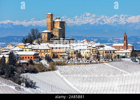 Piccola città medievale e i vigneti in collina innevate come mountain range sullo sfondo in Piemonte, Italia settentrionale. Foto Stock