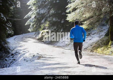Uomo di jogging sul sentiero nella soleggiata, boschi innevati Foto Stock