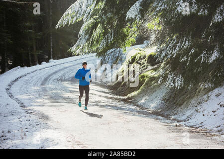 Uomo di jogging sul sentiero nella soleggiata, boschi innevati Foto Stock