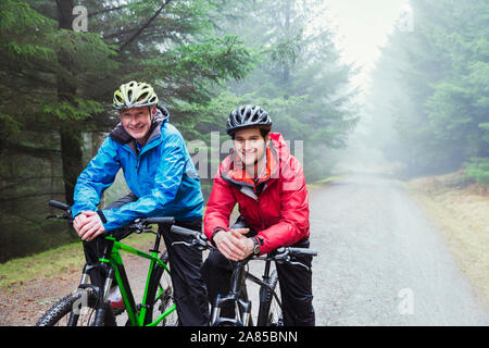 Ritratto felice padre e figlio mountain bike sul sentiero nel bosco di pioggia Foto Stock