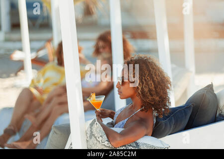 Giovane donna di rilassarsi con un cocktail sulla spiaggia patio Foto Stock