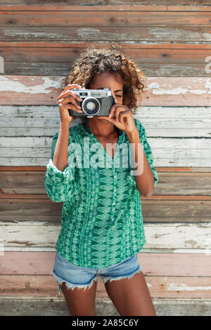 Ritratto di giovane donna con fotocamera retrò contro asse di legno parete