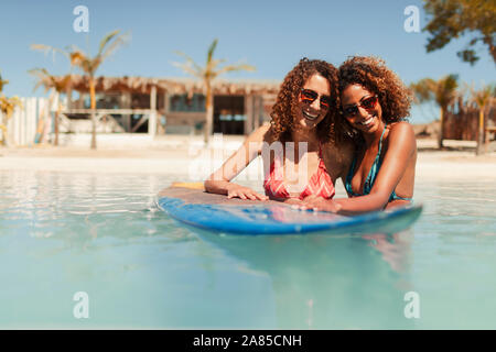 Ritratto felice di donne giovani amici con la tavola da surf nella soleggiata ocean Foto Stock