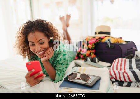 Giovane donna con smart phone disimballaggio valigia sul letto Foto Stock