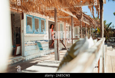 Donna in bikini in piedi nella porta di sunny beach hut Foto Stock