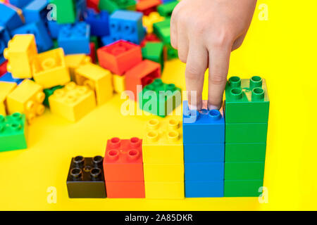 Dita fino a piedi su pile di grafici a barre in plastica blocchi di costruzione di mattoni giocattolo su sfondo giallo. Foto Stock