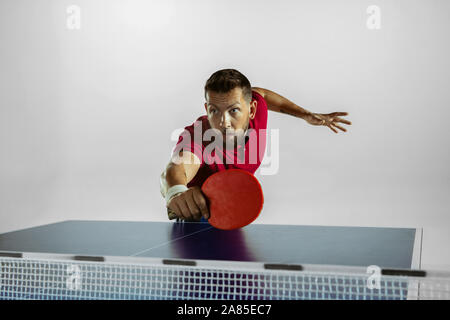 Forte. Giovane uomo gioca ping pong su bianco di sfondo per studio. Il modello riproduce il ping pong. Concetto di attività per il tempo libero, lo sport, le emozioni umane nel gioco, uno stile di vita sano, motion, azione, movimento. Foto Stock