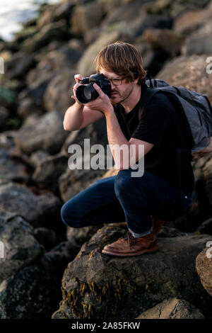 Giovane uomo fotografia ripresa mentre accovacciato su pietra Foto Stock