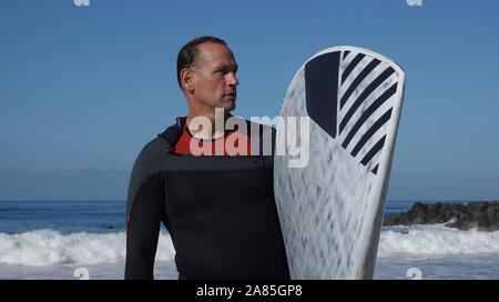 Athletic uomo (52 anni) Caucasica permanente sulla spiaggia tenendo la sua SUP (Stand Up Paddle board) Foto Stock