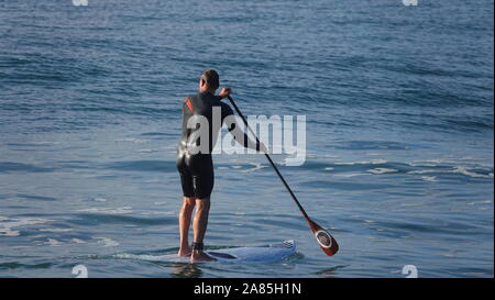 Athletic uomo (52 anno vecchio Caucasica) le piastre piane di acqua oceanica su un SUP (Stand Up Paddle board) Foto Stock