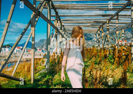 Bella ragazza in abito bianco in posa in prossimità di essiccatori di pesce in Henningsvaer, Isole Lofoten in Norvegia Foto Stock