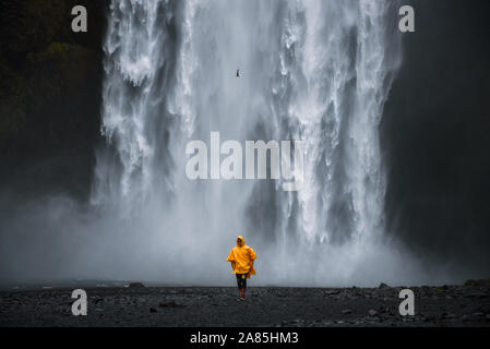 Tourist indossando un impermeabile giallo passeggiate dall'Skogafoss cascata in Islanda Foto Stock