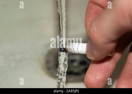 Sigaretta in una mano d'uomo spenta sotto un flusso di acqua concetto foto. I pericoli del fumo. Uno stile di vita sano. Rifiuto di cattive abitudini Foto Stock