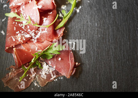 Gustosi piatti appetitosi italiano classico bresaola con rucola e parmigiano su nero ardesia sfondo. Vista da sopra. Vista dall'alto. Posizione orizzontale Foto Stock