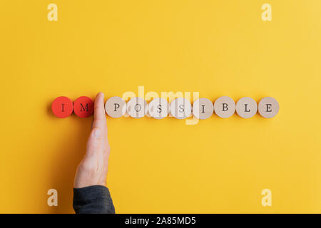 Maschio di separazione a mano lettere IM dalla parola impossibile scritto sul taglio di legno cerchi in una immagine concettuale. Su sfondo giallo. Foto Stock