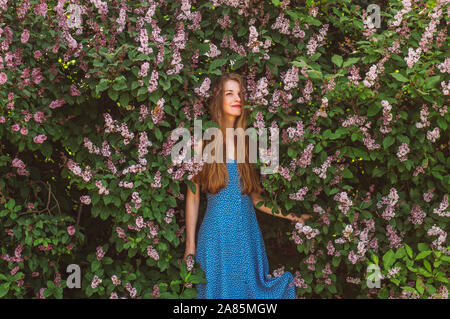 Ritratto di sorridere cercando la ragazza con i capelli biondi e vestito blu tra lilla, estate Foto Stock