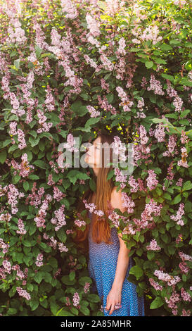 Ritratto di una ragazza con i capelli biondi e vestito blu che sentire il profumo dei fiori tra lilla, estate Foto Stock