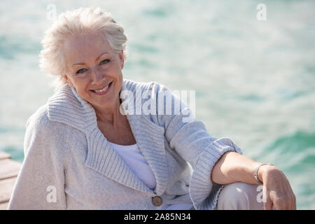 Attraente senior donna seduta su un molo Foto Stock
