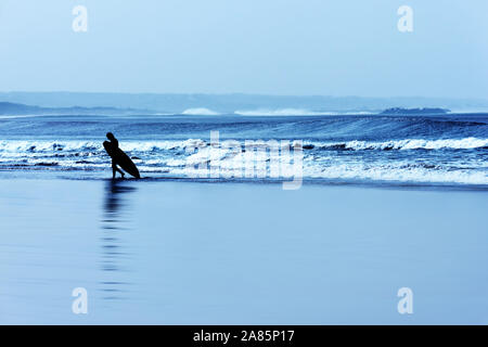 Un surfista cammina con la sua tavola da surf sulla spiaggia di Essaouira. Foto Stock