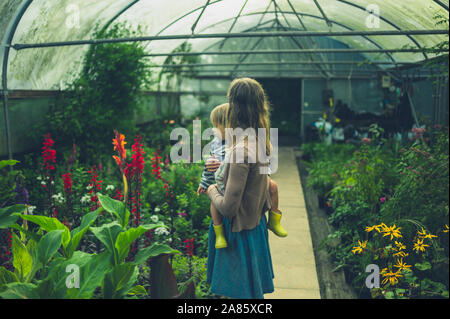 Una giovane madre sta esplorando una serra con il suo bambino nelle braccia Foto Stock