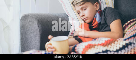 Ragazzo malato a letto con coperta di lana, bottiglie di acqua calda e di una tazza alta. Triste teen con l'influenza si appoggia a casa da solo in una fredda giornata invernale. Bambino con ingredienti di stagione Foto Stock