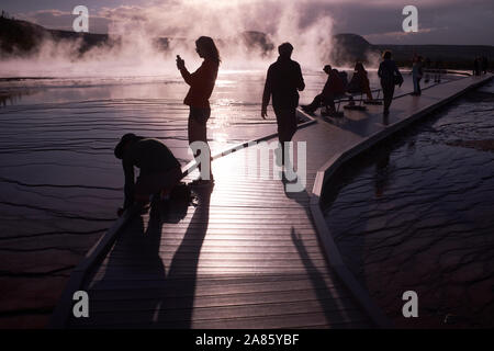 I visitatori si stagliano contro il sole e la crescita del vapore a Grand Prismatic Hot Springs nel Parco Nazionale di Yellowstone, Wyoming USA Foto Stock