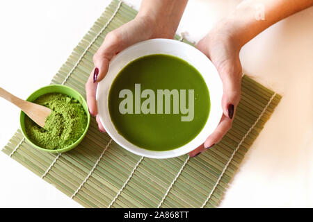 Il cucchiaio di legno con polvere di tè verde Matcha nella tazza, isolati su sfondo bianco. Foto Stock