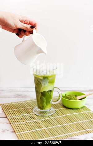 Iced matcha latte drink nel bicchiere tumbler con latte di cocco versare dal lanciatore a mano, copia dello spazio. Estate vegano rinfrescanti bevande bevanda fredda. Foto Stock