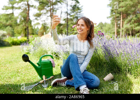 Donna prendendo selfie tramite smartphone nel giardino estivo Foto Stock
