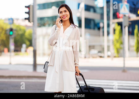 Donna con borsa da viaggio chiamando sul cellulare in città Foto Stock