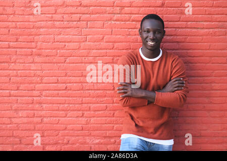 Ritratto di giovane africano un uomo Guarda la fotocamera e sorridente. Copia spazio sulla Parete Rossa in background. Foto Stock