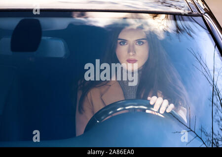 Una giovane donna seduta in una vettura dietro la ruota.sta andando andare. nel vetro della vettura riflesso del cielo. Foto Stock
