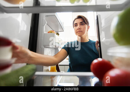 Donna prendendo il cibo dal frigo a casa Foto Stock