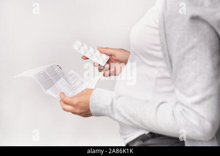 Irriconoscibile Donna Incinta Azienda pillole Leggere le istruzioni di medicazione, sfondo bianco Foto Stock