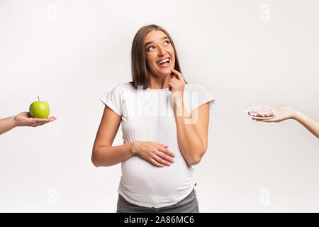 Donna incinta scegliendo tra Apple e la ciambella in piedi, Studio Shot Foto Stock