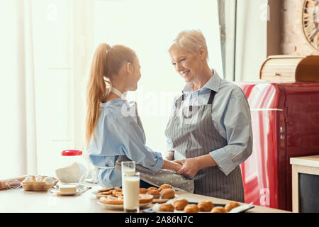 Gentile ragazza e la nonna di conversazione mentre mangiando in cucina Foto Stock