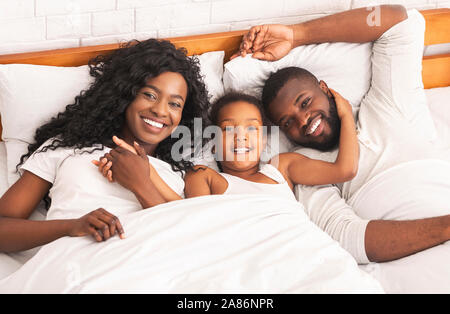 Felice afro i genitori e la loro figlia abbracciando insieme a letto Foto Stock