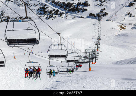 Pirenei, Andorra - 15 febbraio 2019: turisti atleti sciatori e snowboarder sulla seggiovia di una stazione sciistica. La linea di sollevamento si estende attraverso t Foto Stock