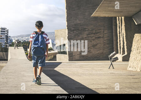 Vista posteriore di un giovane ragazzo con zaino, passeggiando in un contesto urbano. Studente alla moda a piedi al di fuori del college dopo un giorno di scuola. La gioventù, nuovo gene Foto Stock