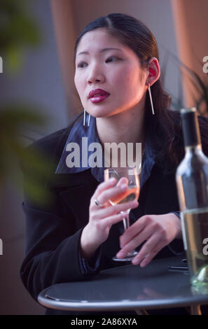 Attraente donna asiatica seduto da solo in un bar tavola con un bicchiere di vino Foto Stock