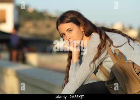 Grave ragazza casual ti guarda al tramonto seduti in strada Foto Stock